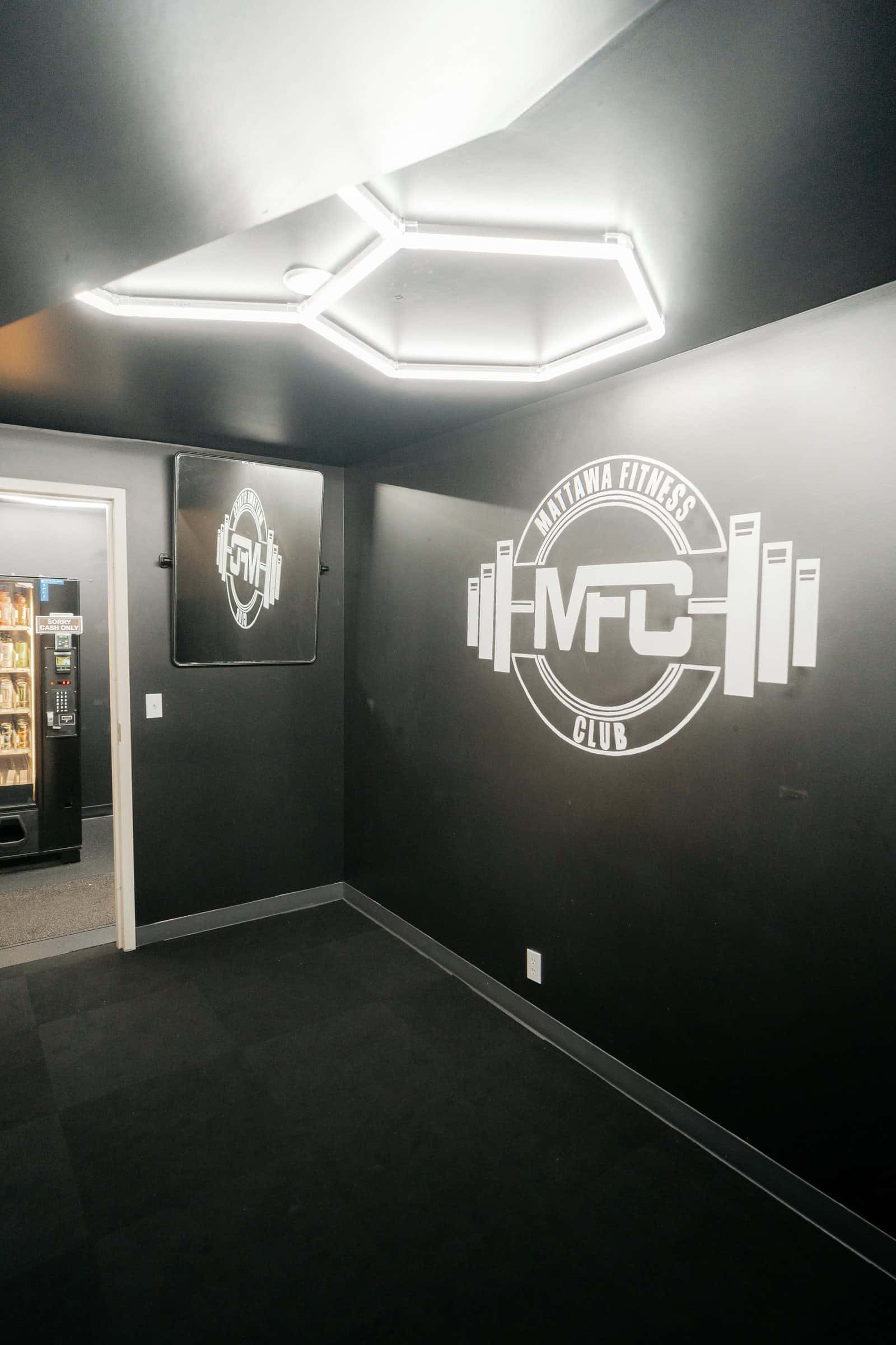 El cuarto de poses: paredes negras, luces hexagonales en el techo y el logo de MFC
